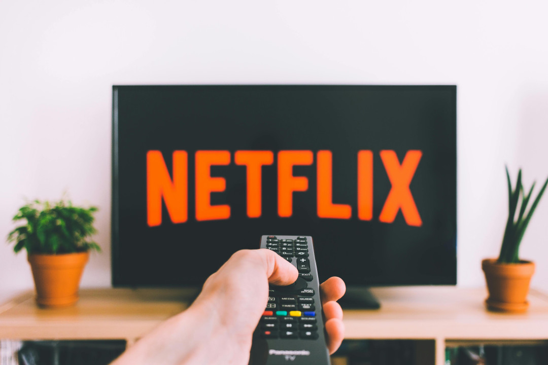 hand-holding-remote-control-in-front-of-tv-with-netflix-image