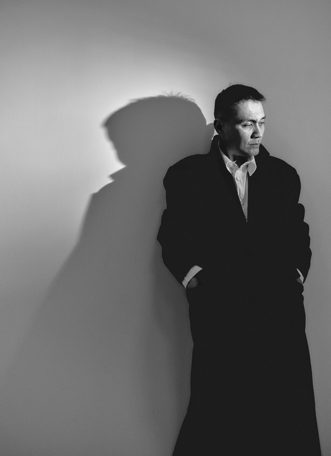 black-and-white-portrait-of-film-director-standing-against-wall-with-shadow-image