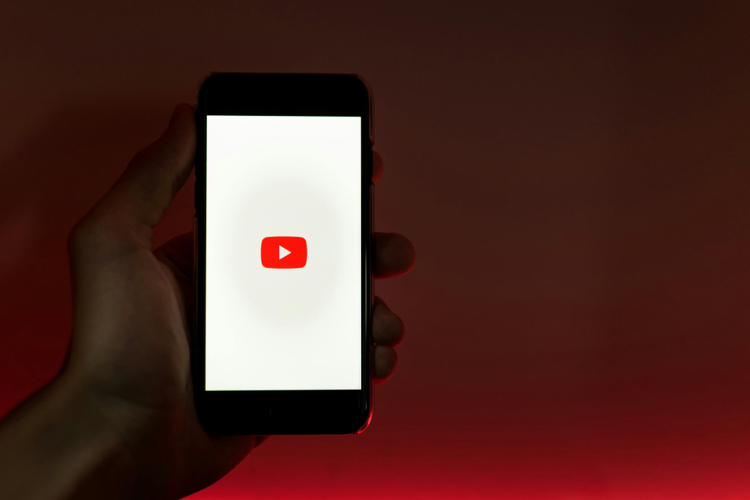 hand-holding-smartphone-with-youtube-logo-on-screen-red-background-image